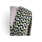 A close-up of a geometric print wrap top on a mannequin torso. The pattern features interlocking shapes in olive green, black, light blue, and cream, with a light beige mannequin visible underneath.