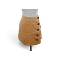 A tan faux suede wrap mini skirt with a row of black buttons, displayed on a white mannequin torso against a white background.