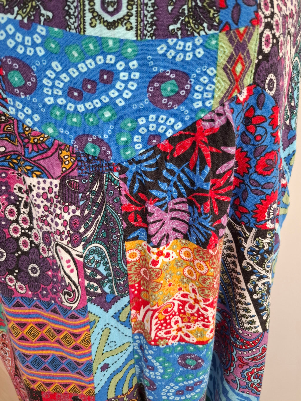 A close-up of a highly patterned patchwork garment featuring multiple colorful prints including paisley, floral, and tropical motifs in blue, red, purple, black, and orange.