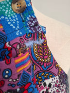 Close-up of a colorful patchwork fabric garment with a brown button, featuring vibrant blue, pink, purple, yellow, and red patterns on a light beige mannequin torso.