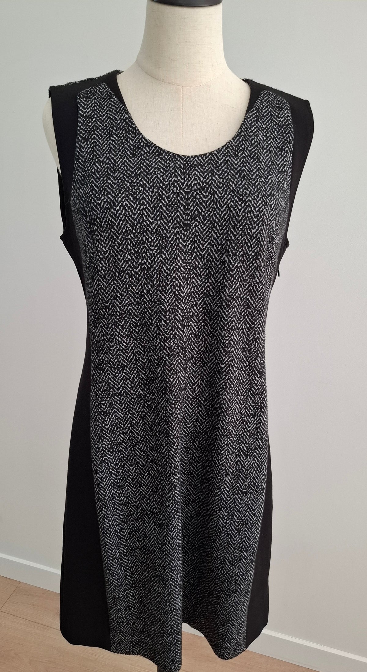 A sleeveless black and gray herringbone knit dress displayed on a mannequin torso against a plain light gray wall.