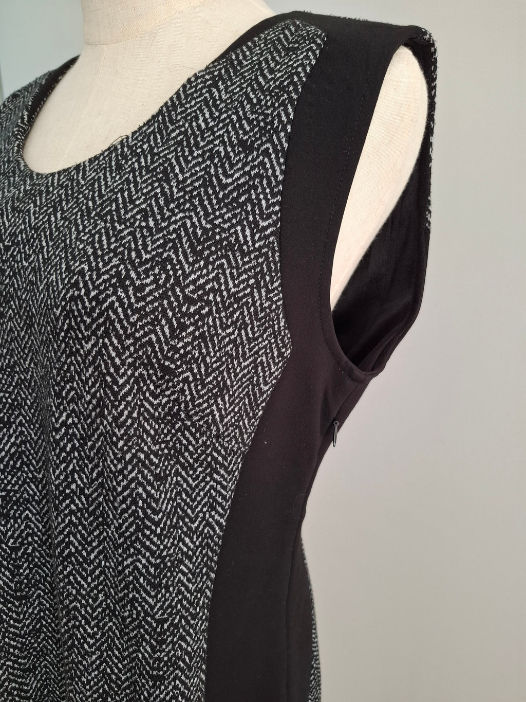 A sleeveless black and white herringbone patterned top with solid black side panels, displayed on a cream-colored dress form against a light gray background.