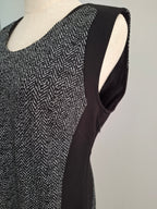 A sleeveless black and white herringbone patterned top with solid black side panels, displayed on a cream-colored dress form against a light gray background.