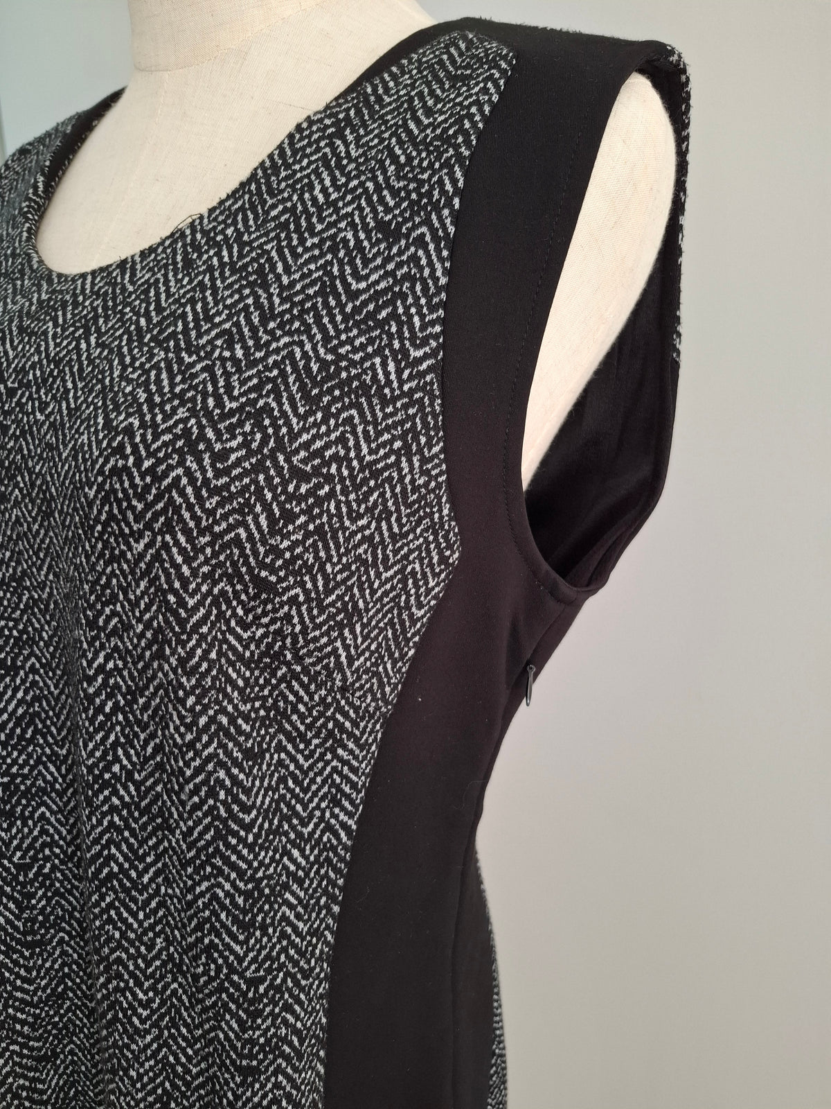 A sleeveless black and white herringbone patterned top with solid black side panels, displayed on a cream-colored dress form against a light gray background.