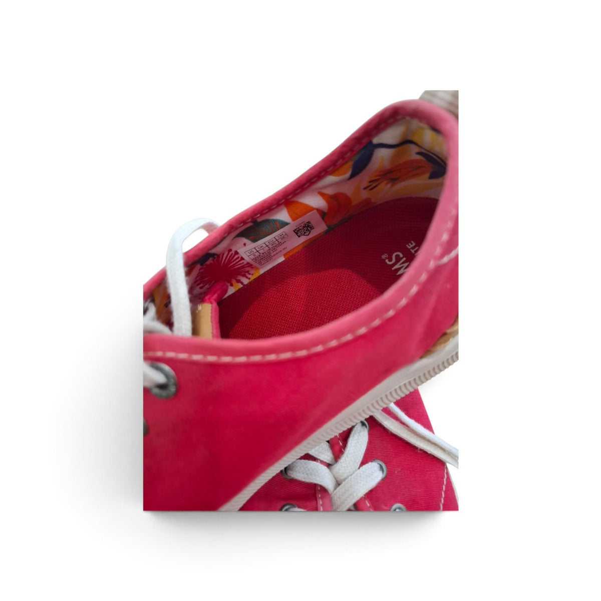 A close-up of a pink canvas sneaker showing the interior lining, white laces, metal eyelets, and a floral pattern on the inner collar, set against a plain white background.
