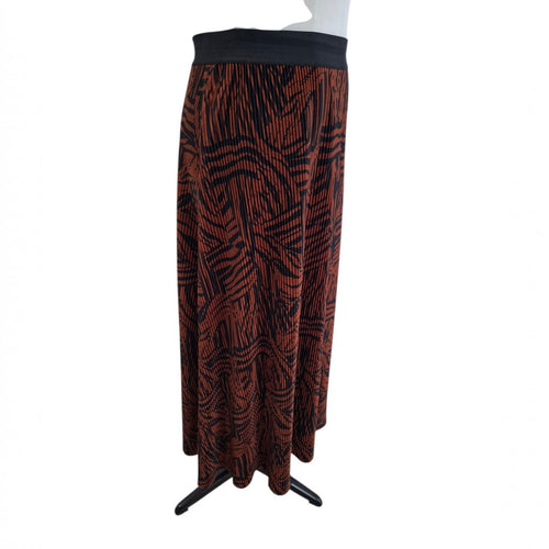 A long pleated skirt with a black and rust-orange abstract pattern, displayed on a white mannequin torso against a white background.