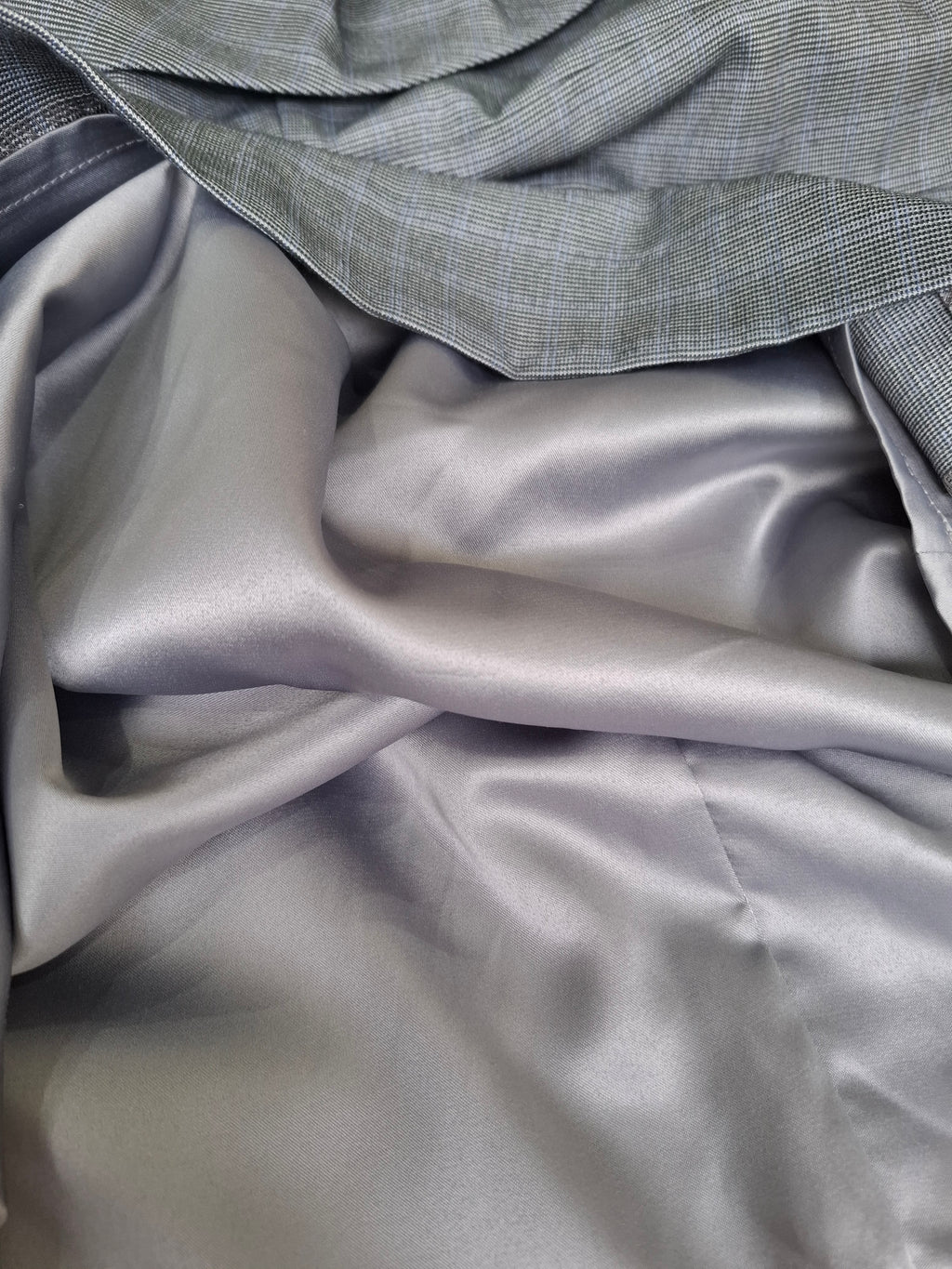 A close-up of draped gray fabric, showing a smooth satin-like lower layer and a textured woven top layer in a matching gray tone.