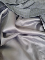 A close-up of draped gray fabric, showing a smooth satin-like lower layer and a textured woven top layer in a matching gray tone.