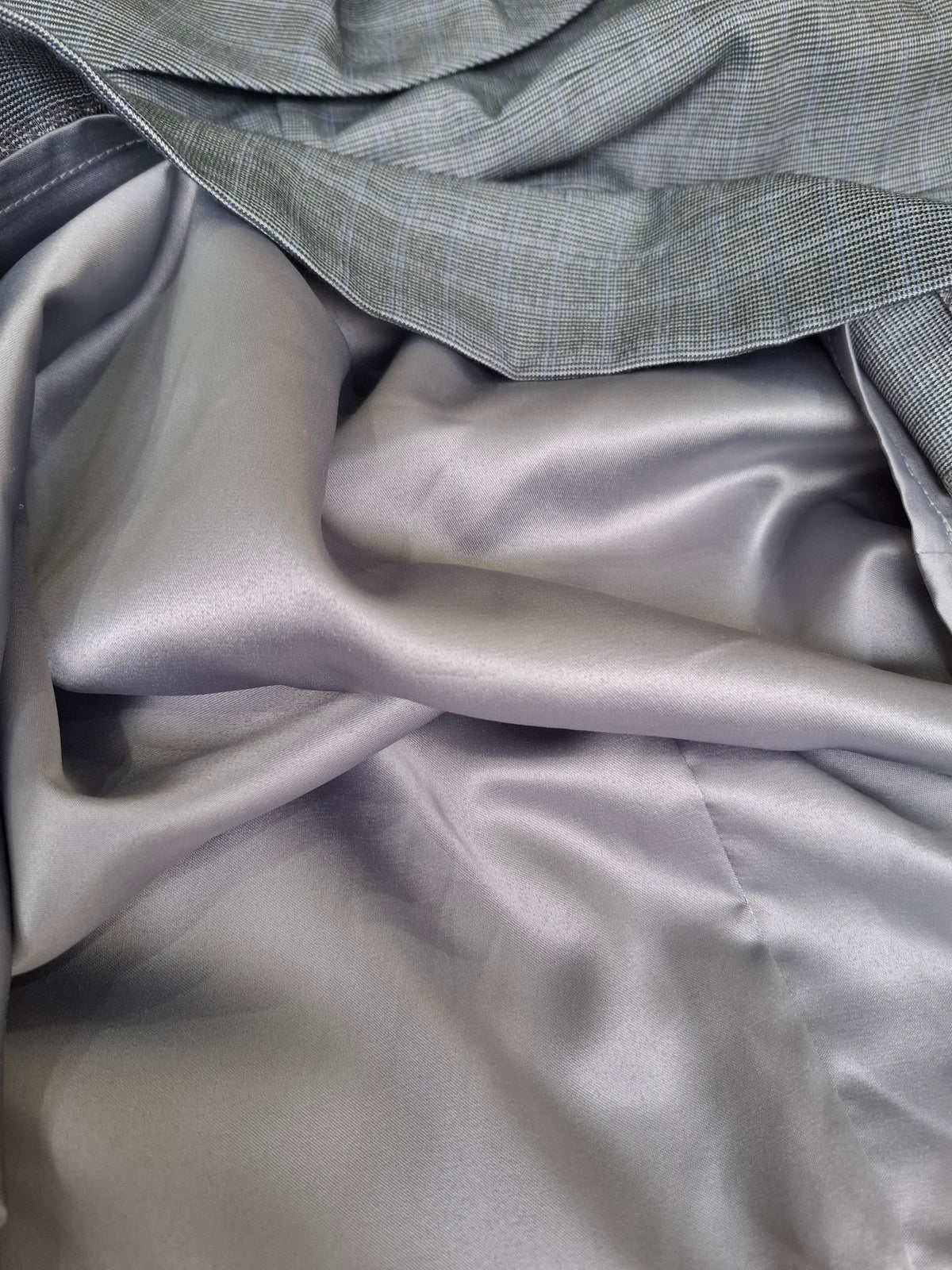 A close-up of draped gray fabric, showing a smooth satin-like lower layer and a textured woven top layer in a matching gray tone.