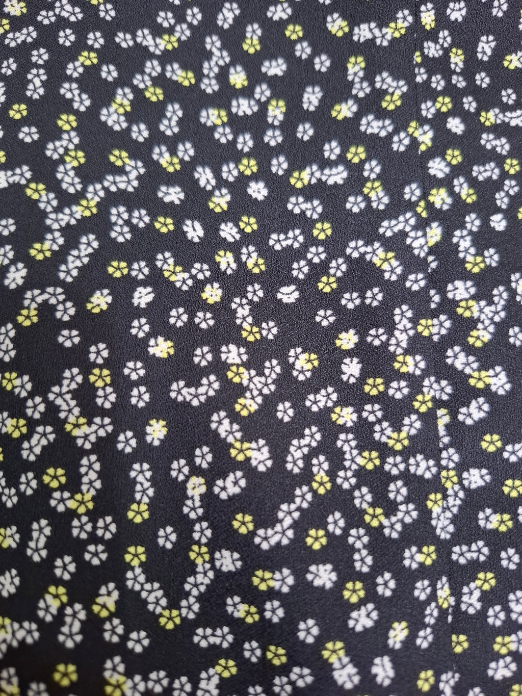 A close-up of a dark charcoal gray or black fabric with a dense, small-scale floral print in white and yellow.