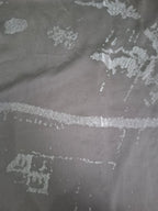 A close-up of a dark gray textured fabric with a distressed, peeling pattern revealing a lighter silver-gray layer underneath.
