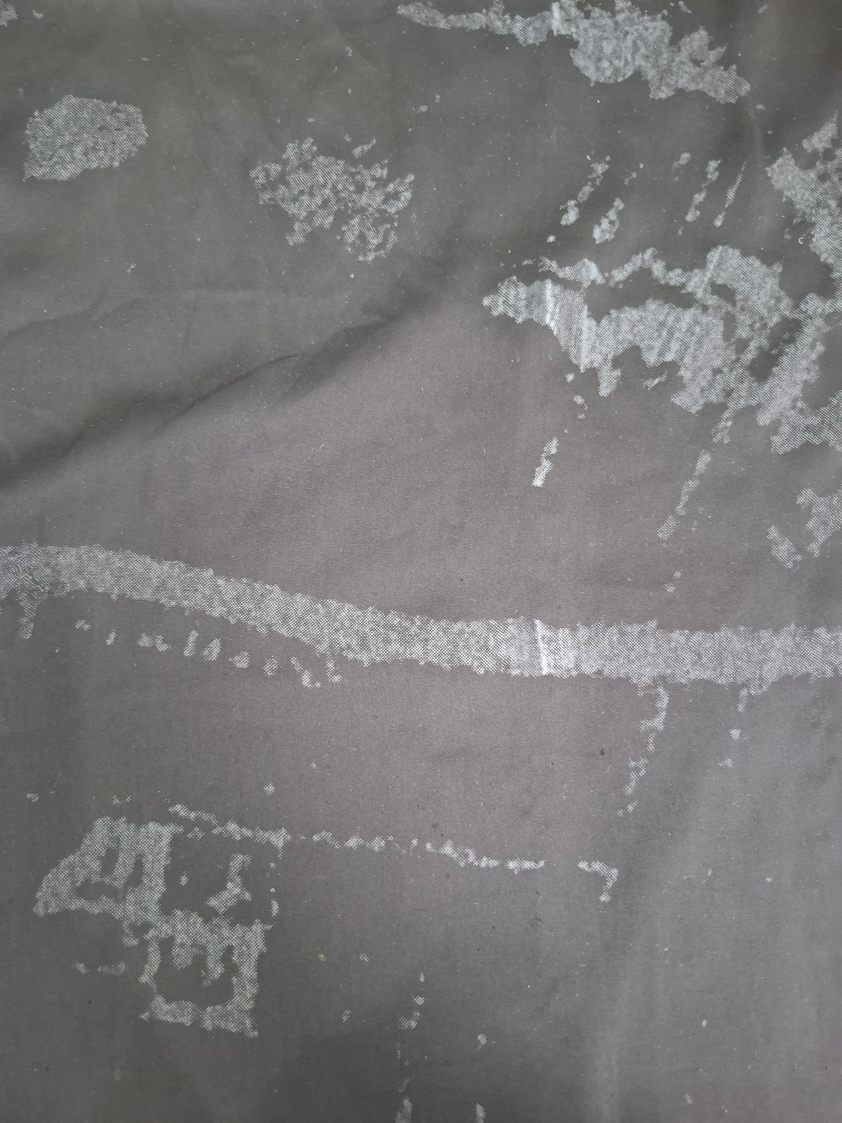 A close-up of a dark gray textured fabric with a distressed, peeling pattern revealing a lighter silver-gray layer underneath.
