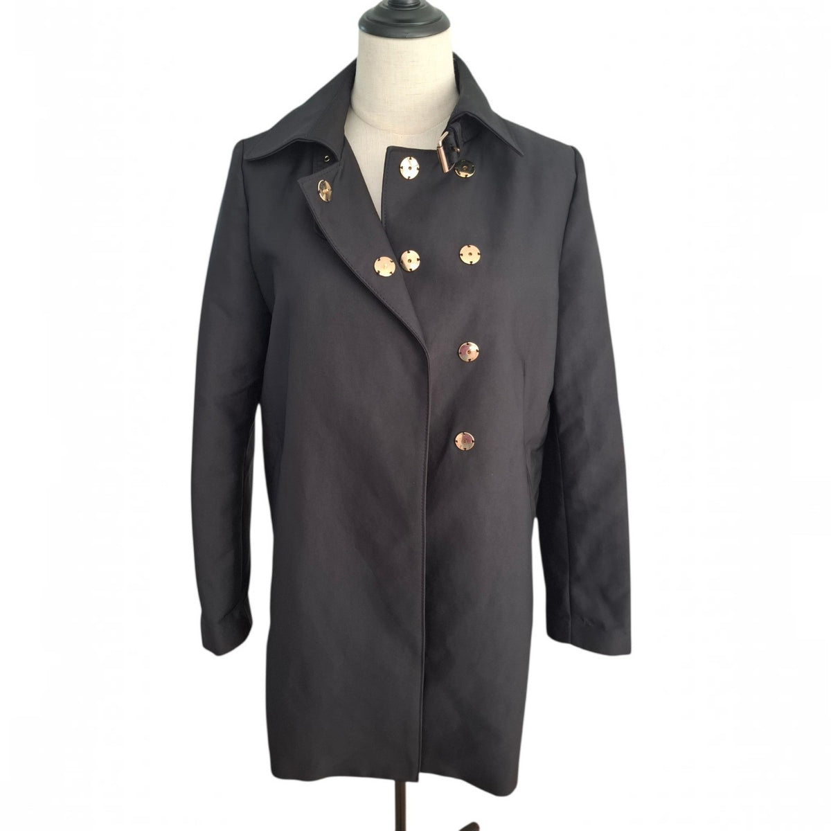 A black double-breasted coat with decorative gold-tone buttons, displayed on a mannequin torso against a plain white background.