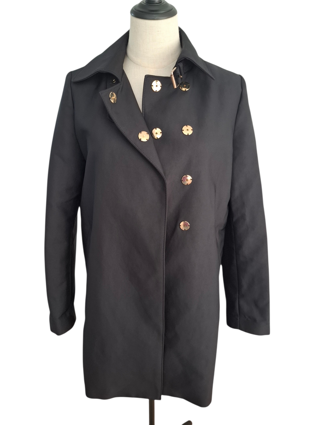 A black double-breasted coat with decorative gold-tone flower-shaped buttons, displayed on a dress form mannequin against a white background.