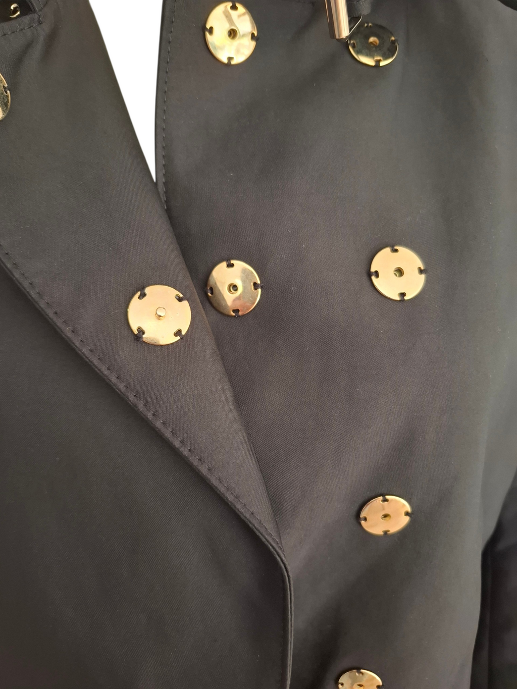 Close-up of a dark charcoal gray double-breasted blazer with prominent round gold-tone metal buttons.