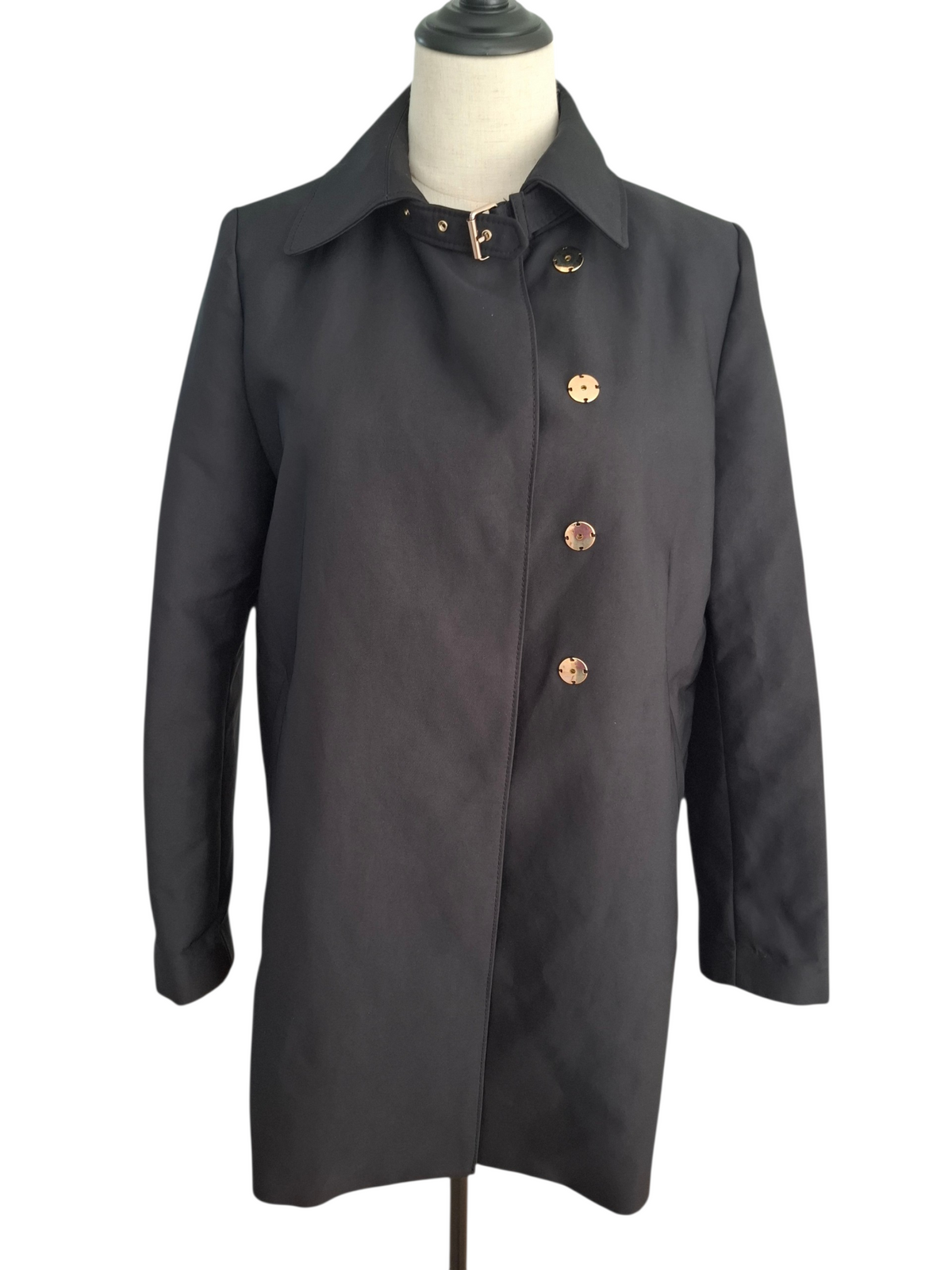 A black trench coat with decorative gold-tone buttons and a collar, displayed on a dress form mannequin against a white background.