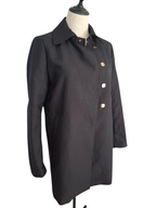 A black longline coat with gold-tone buttons, displayed on a cream mannequin torso against a white background.