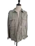 A light olive green military-style utility jacket displayed on a cream-colored dress form mannequin against a plain white background.