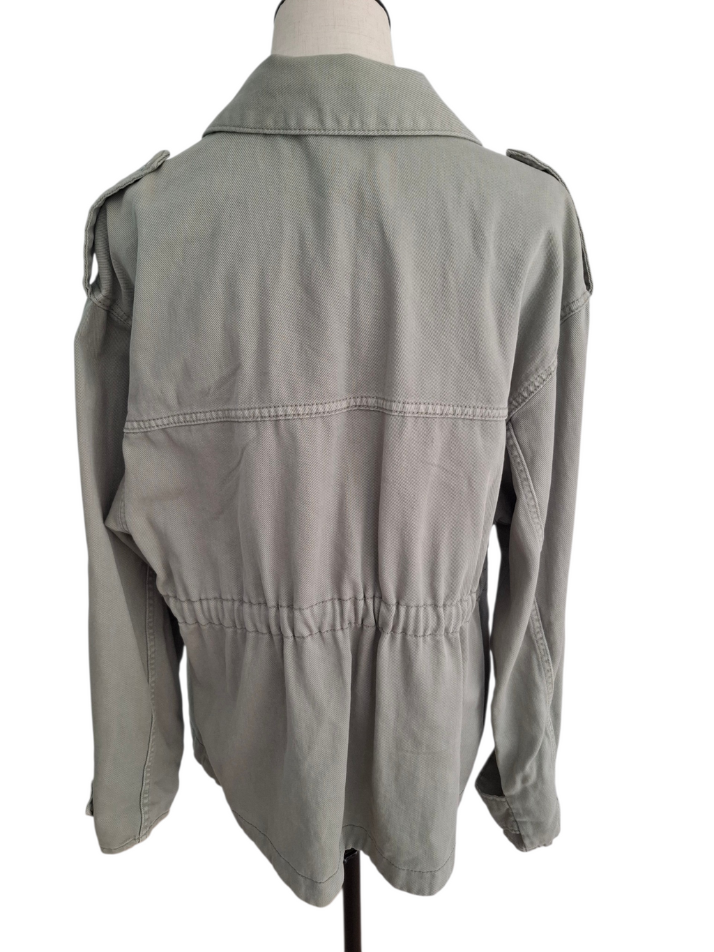 A light gray utility jacket with shoulder epaulets and a gathered waist, displayed on a mannequin from the back against a white background.