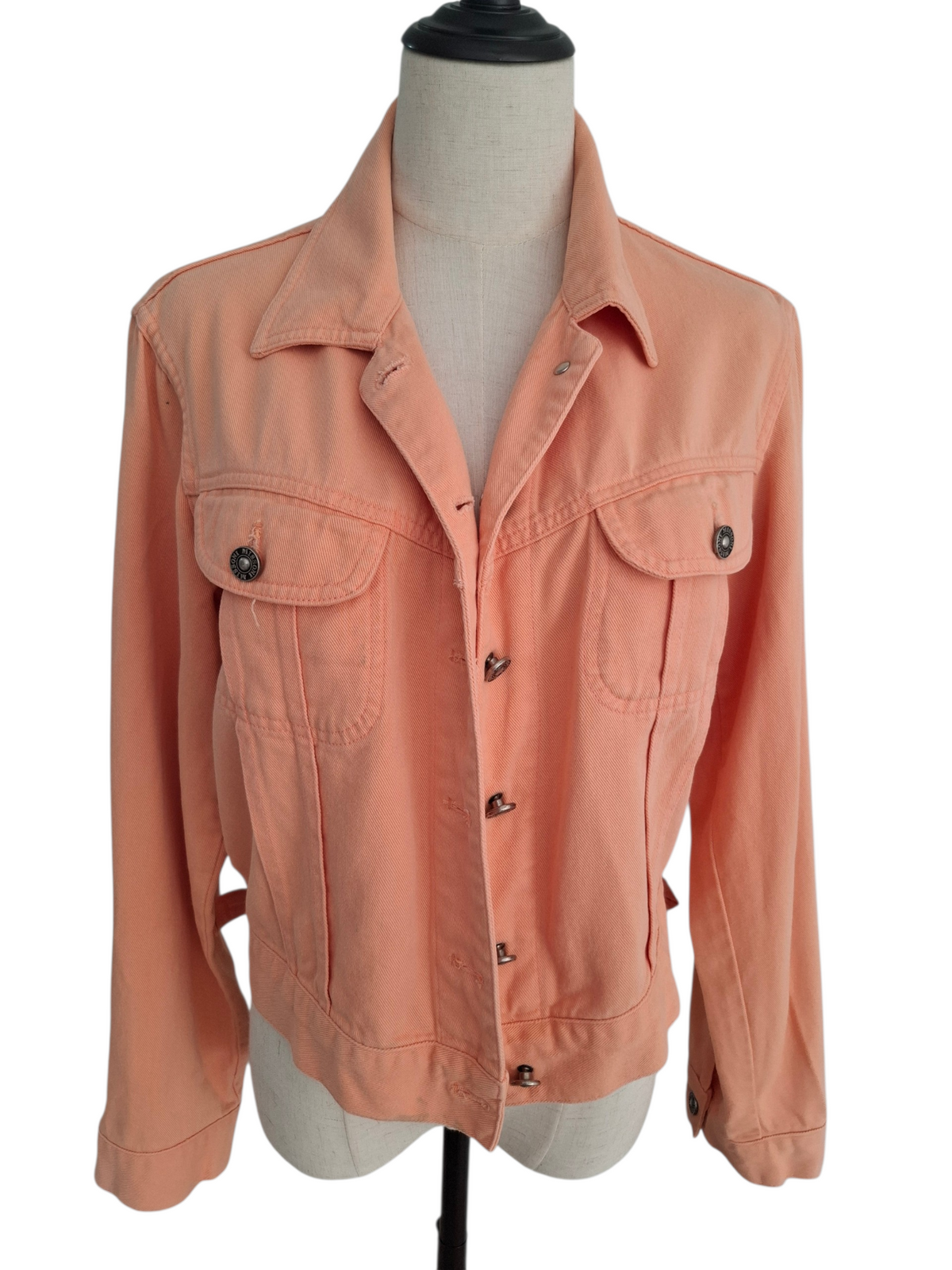 A peach-colored denim jacket displayed on a cream-colored dress form mannequin against a plain white background.