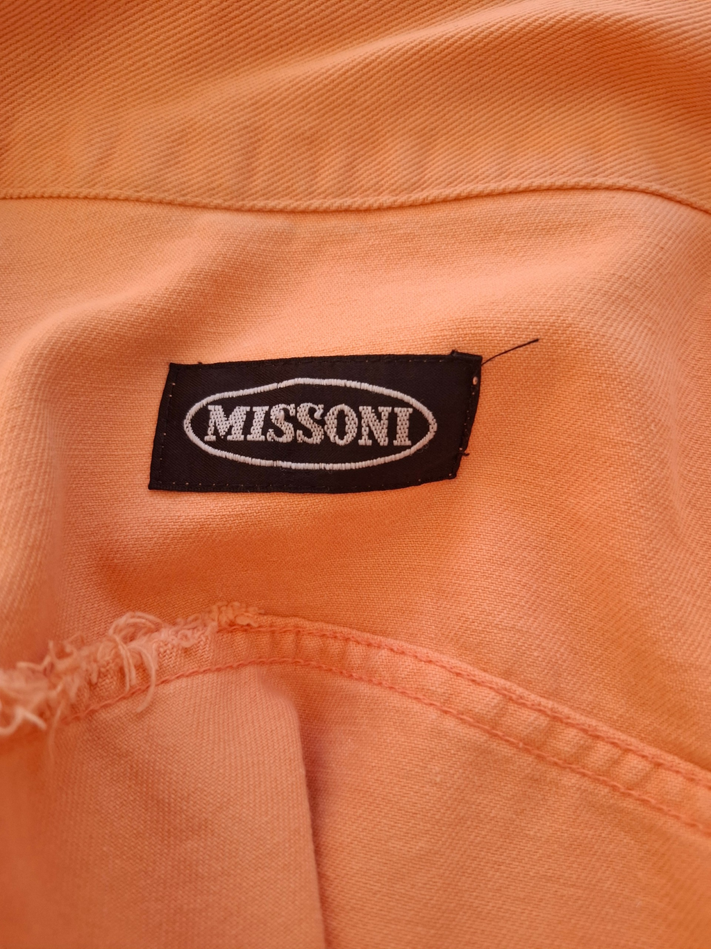 Close-up of a peach-colored woven fabric garment with a black embroidered Missoni brand label stitched onto the chest.