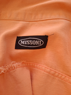 Close-up of a peach-colored woven fabric garment with a black embroidered Missoni brand label stitched onto the chest.