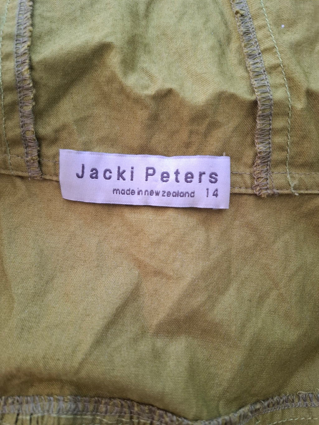 Close-up of a vintage olive green Jacki Peters garment with a white paper brand label sewn onto the inside.