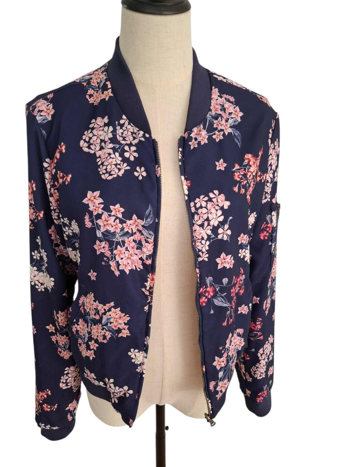 A navy blue satin bomber jacket with a pink and white floral print, displayed on a beige dress form mannequin against a white background.