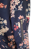 Close-up of a floral-patterned garment sleeve or jacket panel in navy blue, featuring pink and peach flowers with a vertical zip pocket and a metal zipper pull.