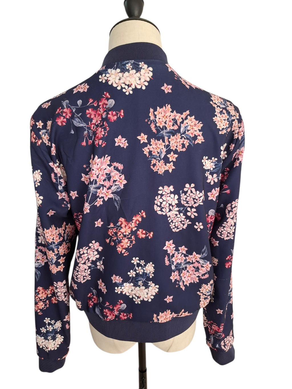 A navy blue bomber jacket with a pink and white floral print, displayed on a mannequin from the back against a white background.