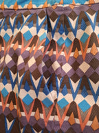 Close-up of a geometric patterned fabric with repeating diamond and chevron motifs in blue, brown, purple, orange, and off-white.