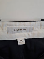 Close-up of the waistband of Country Road trousers, showing a white fabric label with the brand name 'COUNTRY ROAD' and a size tag indicating '14 MADE IN CHINA'. The trousers are black with a white waistband.
