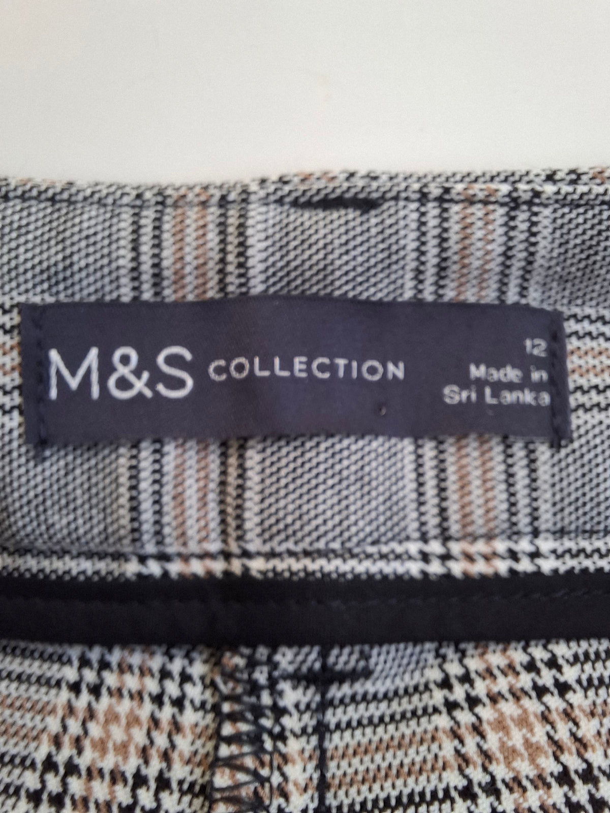 Close-up of a M&S Collection garment label sewn onto a plaid fabric, showing the brand name and 'Made in Sri Lanka' text.