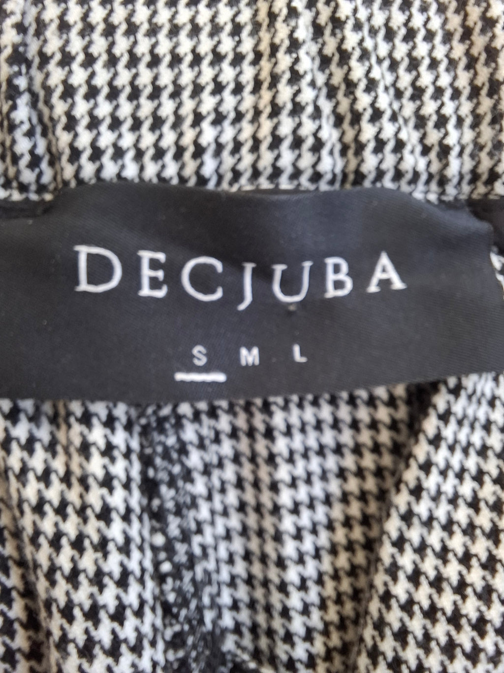 Close-up of a black and white houndstooth patterned garment with a black brand label reading DECJUBA and size S
