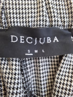Close-up of a black and white houndstooth patterned garment with a black brand label reading DECJUBA and size S