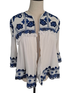 White long-sleeve blouse with blue floral embroidery and ruffle trim, displayed on a mannequin torso against a plain white background.