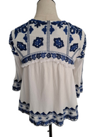 White blouse with blue floral embroidery and lace trim, displayed on a mannequin torso against a white background.