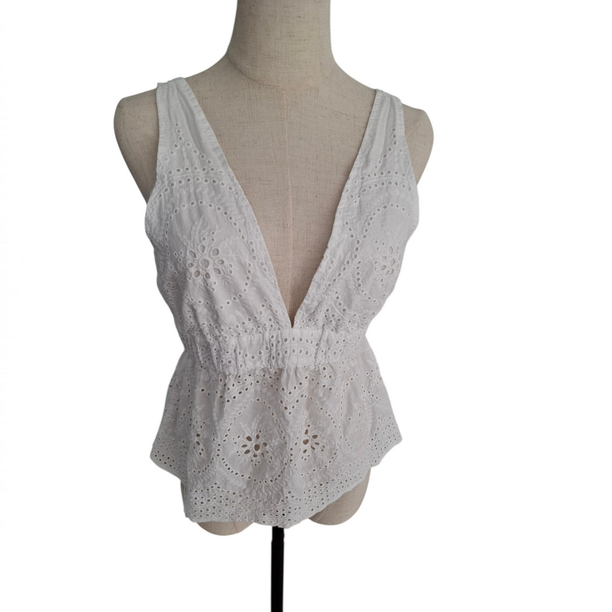 A white sleeveless eyelet lace top with a deep V-neckline, displayed on a beige fabric dress form mannequin against a plain white background.