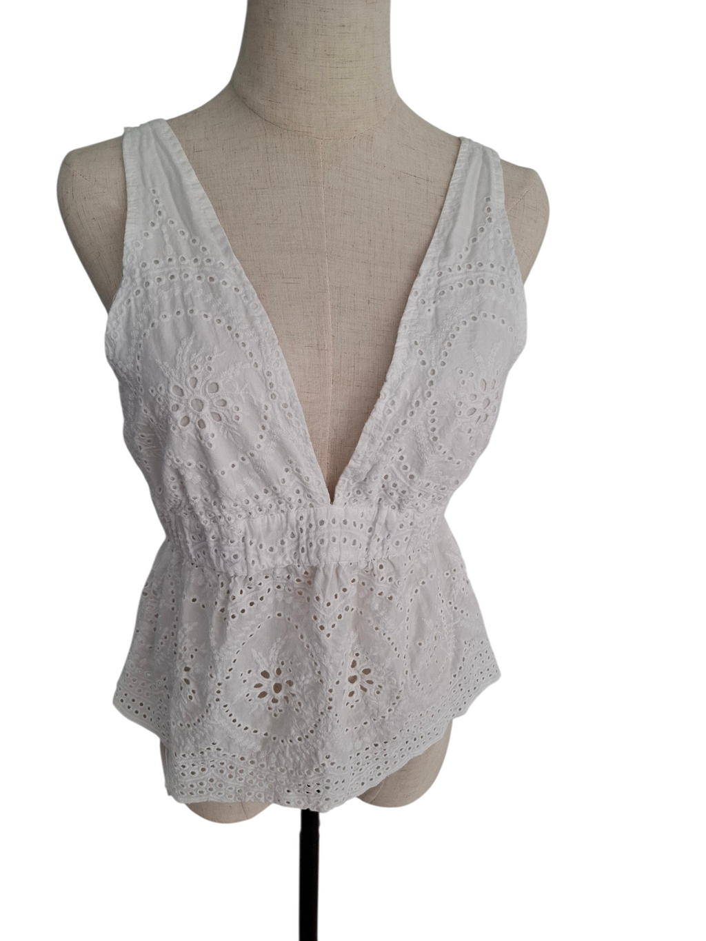 White sleeveless eyelet lace top with a deep V-neckline, displayed on a beige fabric mannequin torso against a plain white background.