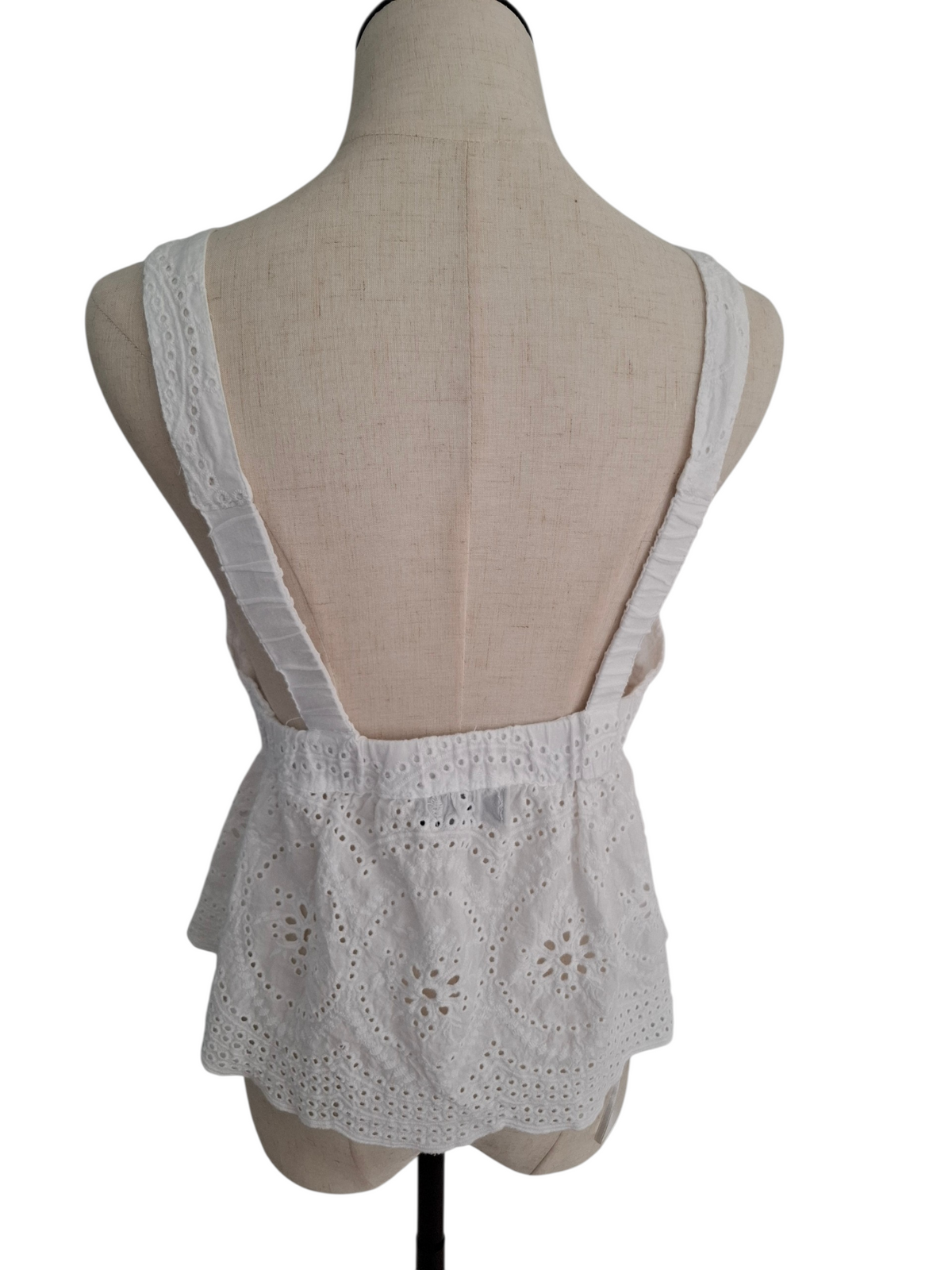 White eyelet lace top with wide shoulder straps and a ruffled peplum hem, displayed on a beige fabric mannequin torso against a white background.
