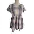 A short-sleeve plaid dress displayed on a mannequin torso against a plain white background. The dress features a cream base with intersecting dark gray, black, and thin pink stripes in a plaid pattern.