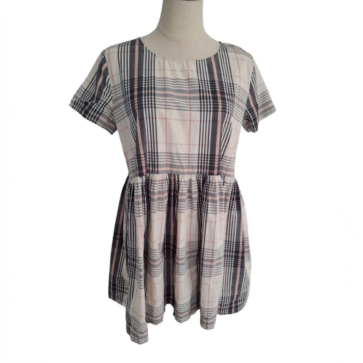 A short-sleeve plaid dress displayed on a mannequin torso against a plain white background. The dress features a cream base with intersecting dark gray, black, and thin pink stripes in a plaid pattern.