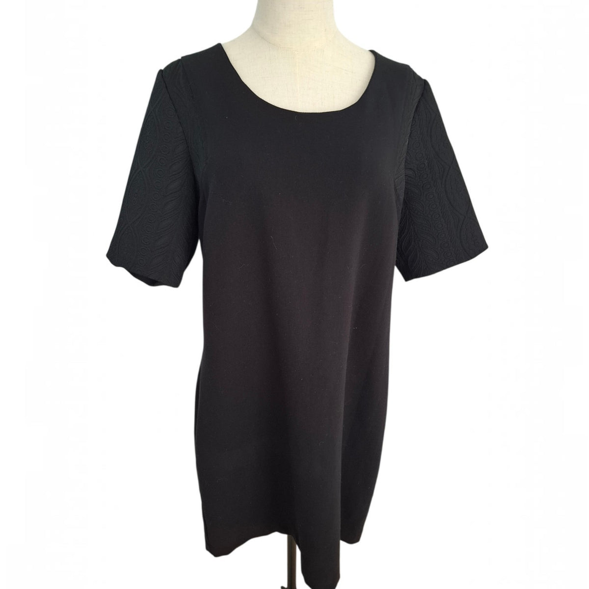 A black short-sleeve tunic top displayed on a cream-colored dress form mannequin against a plain white background.