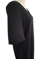 A black V-neck dress or tunic displayed on a mannequin, featuring textured, patterned elbow-length sleeves and a smooth black body, shown against a plain white background.