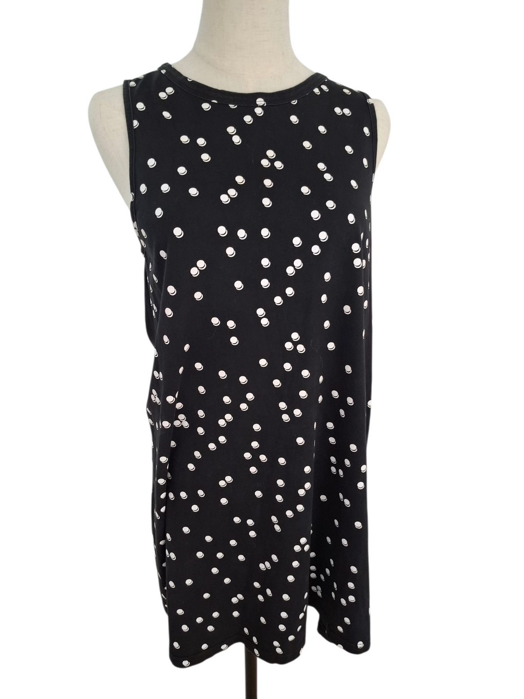 A sleeveless black shift dress with an allover white polka dot pattern, displayed on a cream mannequin torso against a plain white background.