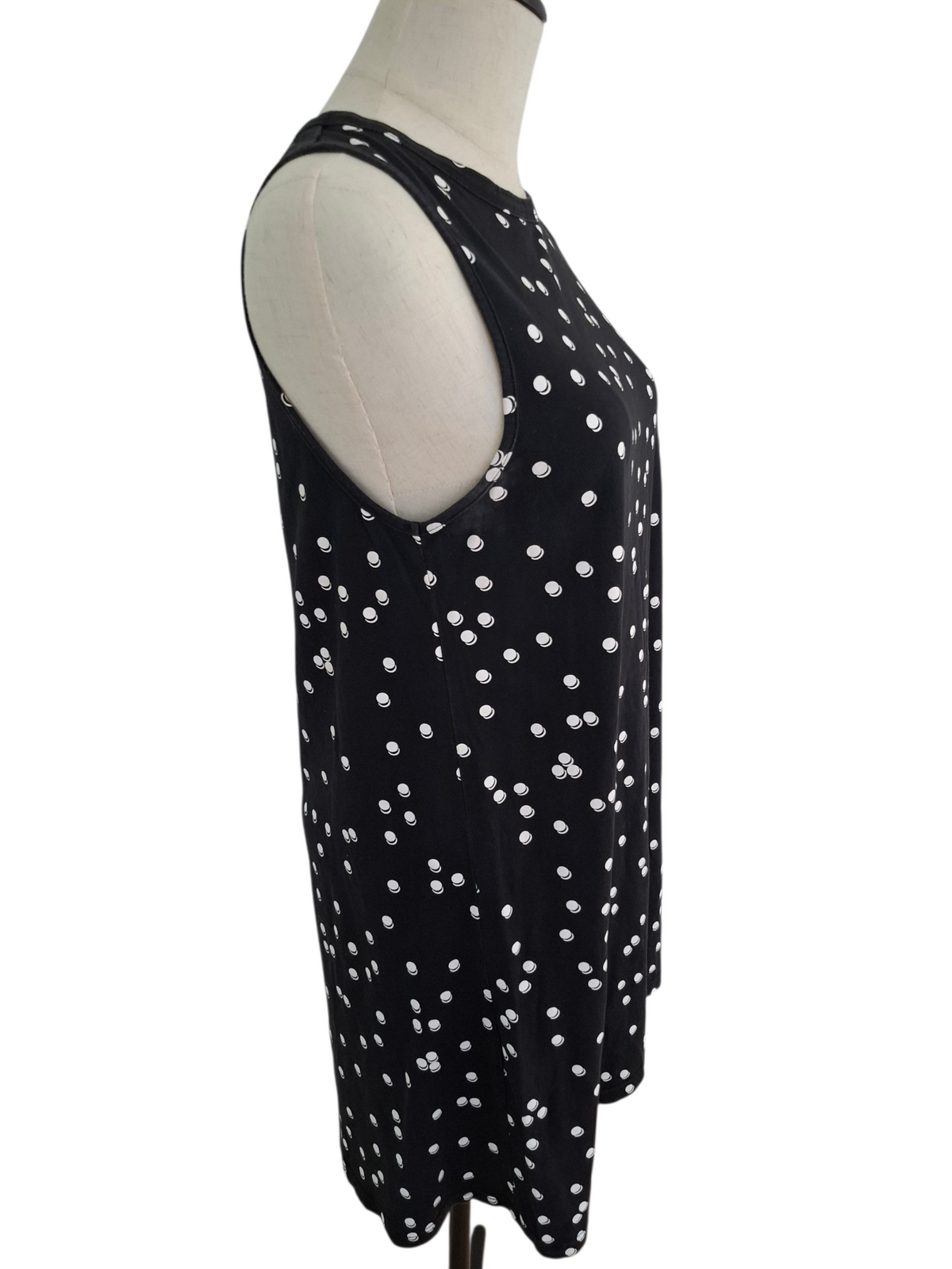A sleeveless black tunic top with a white polka dot pattern, displayed on a cream-colored dress form mannequin against a plain white background.