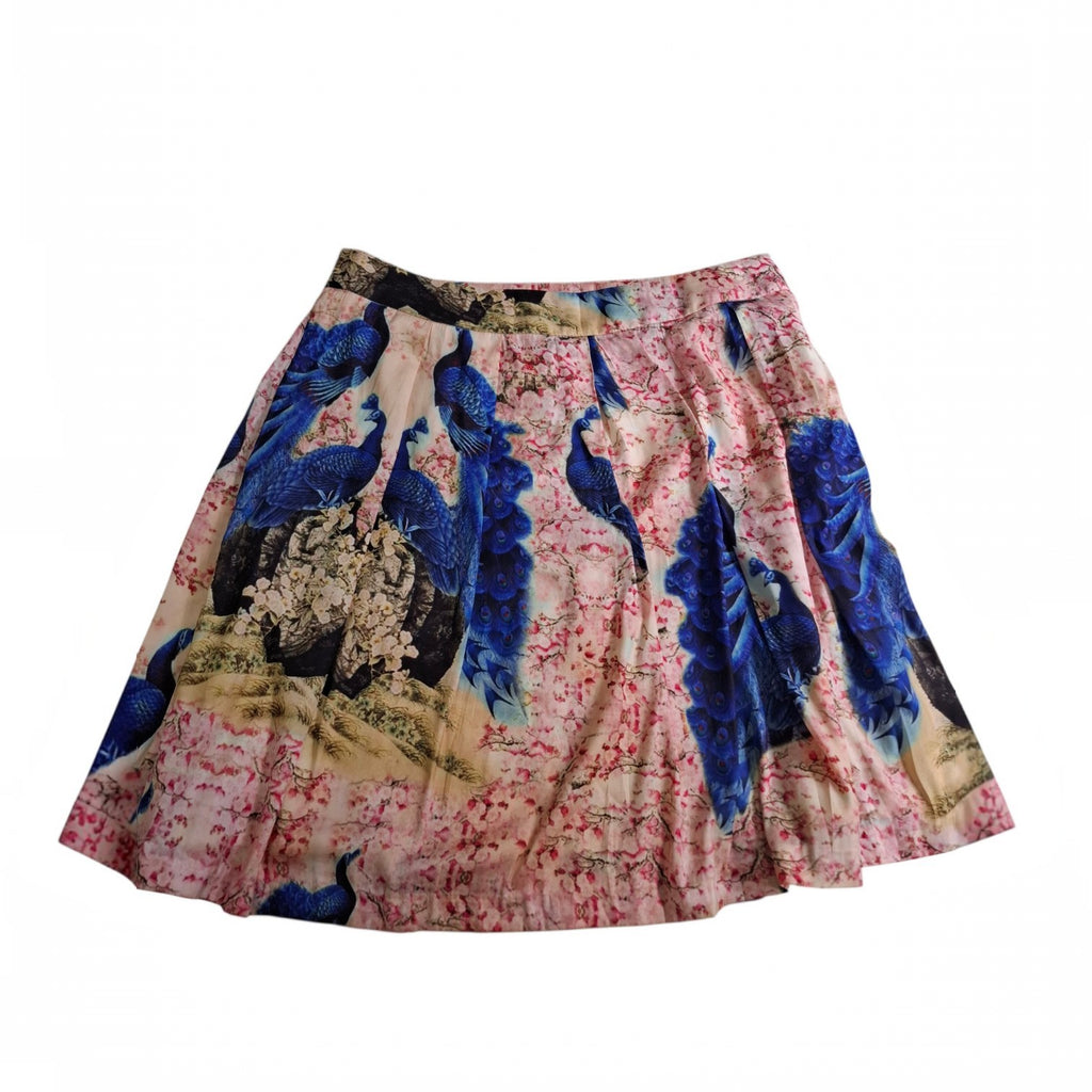 A flared A-line skirt featuring a vibrant peacock print with blue peacocks, pink cherry blossoms, and beige foliage on a white background.