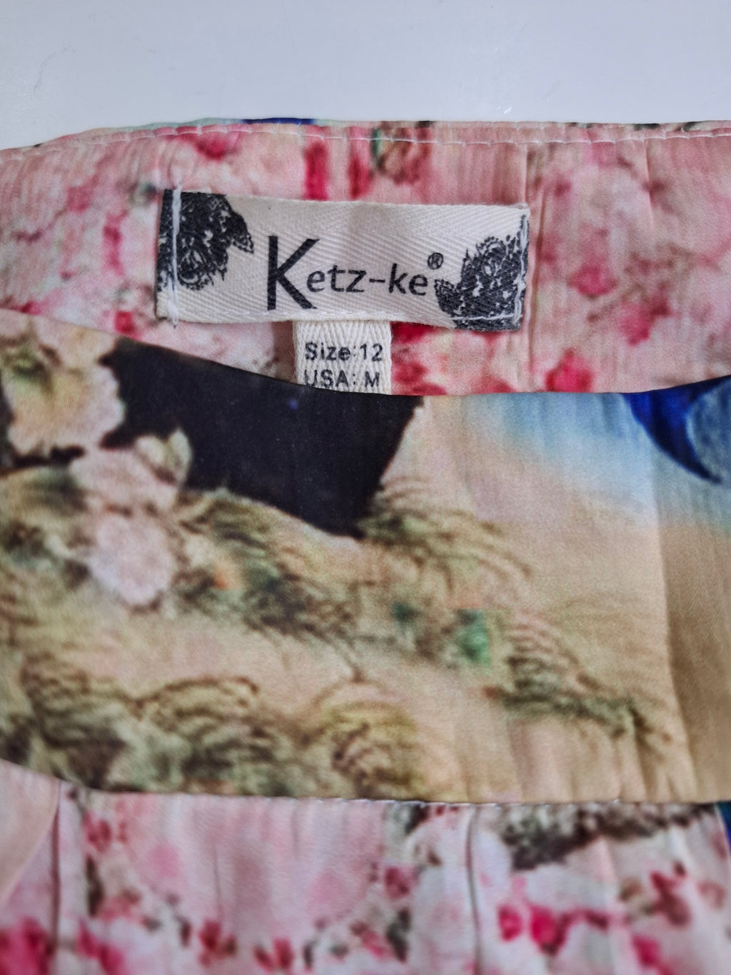 Close-up of a Ketz-ke brand garment label sewn onto a floral printed fabric, showing the size 12 USA-M measurement.
