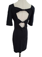 A black short-sleeve dress displayed on a cream mannequin torso, showing a dramatic open back with a large bow detail and cutout.