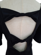 Close-up back view of a black short-sleeve top displayed on a cream fabric dress form, showing a large open back with twisted crossover straps.